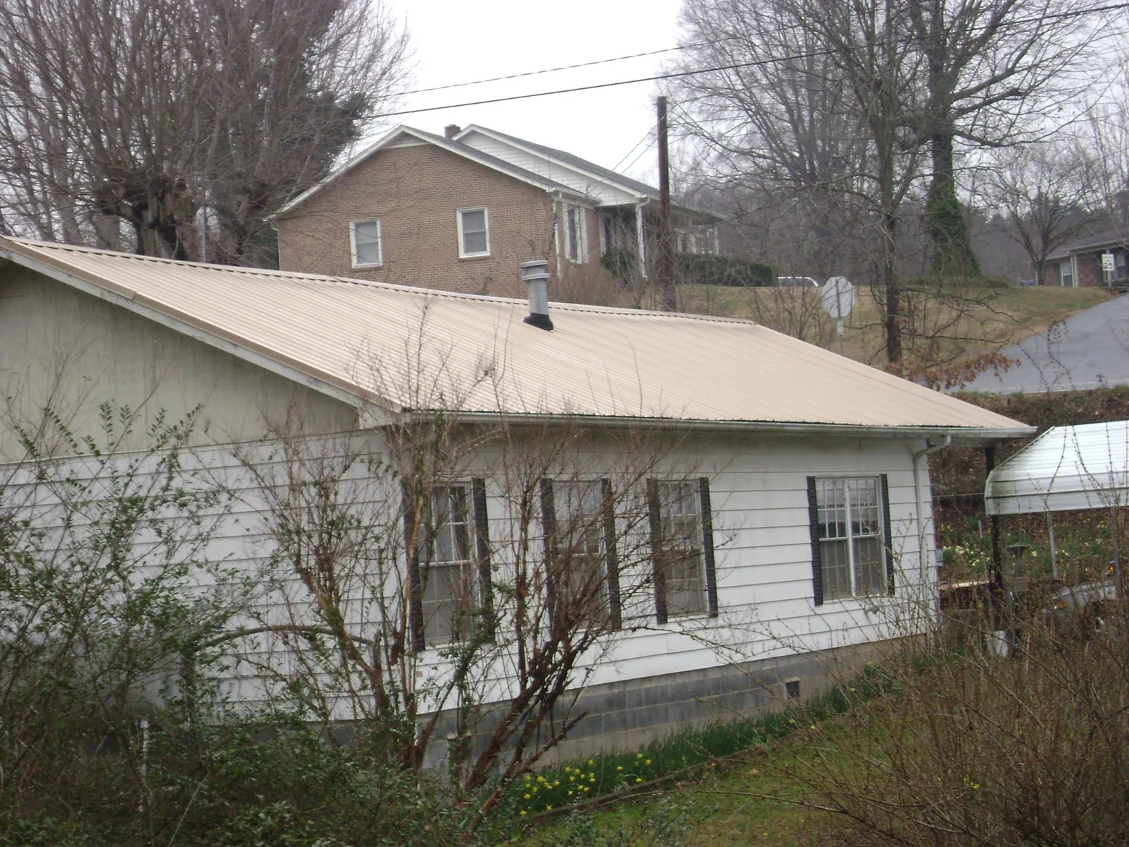 Tan metal roof on a white sided house set into a hillside — Commercial Roofing by Roofing Brothers in Warwick
